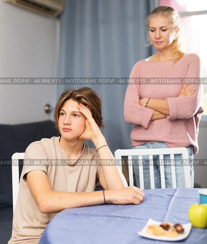 Offended teenager sitting at home table after disagreements with mom. Стоковое фото, фотограф Яков Филимонов / Фотобанк Лори