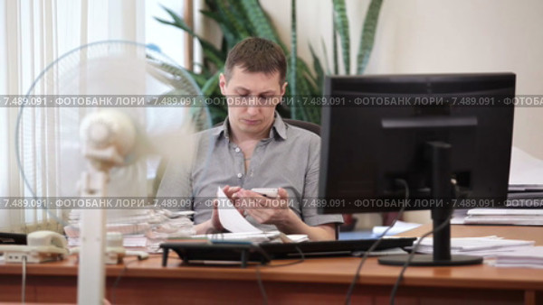 Офисный сотрудник просматривает интернет станицы на мобильном смартфоне на рабочем месте под работающим вентилятором. Стоковое видео, видеограф Кекяляйнен Андрей / Фотобанк Лори