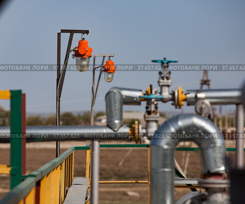 Oil refinery plant in desert. Explosion-proof lamp, valve armature and pipes on grey sky background. Focus on first lamp. Стоковое фото, фотограф Alexey Rezvykh / Фотобанк Лори