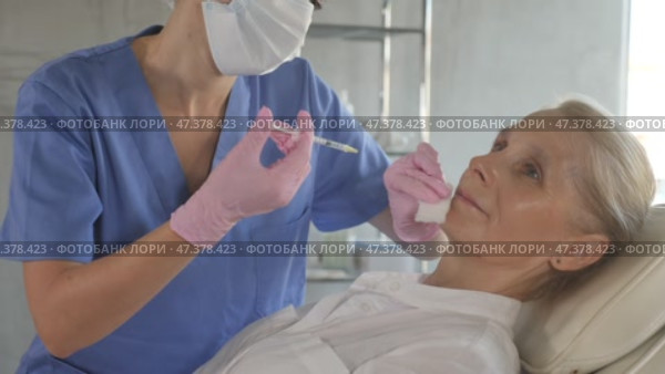 Old female patient lying on clinical chair undergoing face care procedure by injection method. Стоковое видео, видеограф Яков Филимонов / Фотобанк Лори