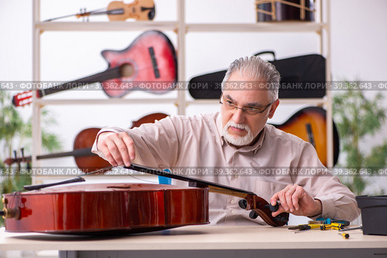 Old male repairman repairing musical instruments at workplace. Стоковое фото, фотограф Elnur / Фотобанк Лори