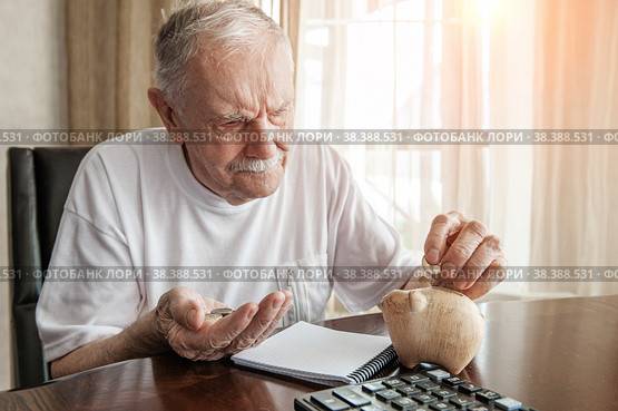 old man in the pandemic counts pennies from the pension fund. Concerned about lockdown, an elderly man puts money in a piggy bank. pensioner calculates the budget of his pension. Стоковое фото, фотограф Оксана Медведева / Фотобанк Лори