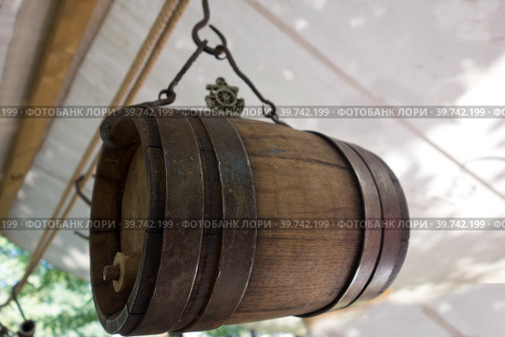 Old wine barrel with iron rings is suspended from a metal hook. Стоковое фото, фотограф Iva Noel / Фотобанк Лори