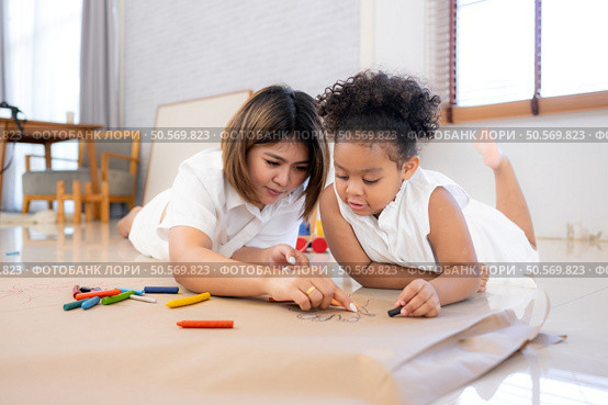 On a holiday, A woman and her little daughters sit on the floor and drawing together in the living room. Стоковое фото, агентство Ingram Publishing / Фотобанк Лори