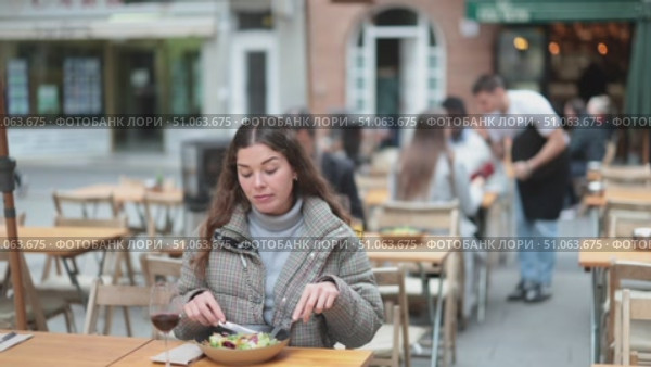 On open area of cafe, girl in restaurant eating salad. Single client sits at table, eats and enjoys views of ancient European city around. Стоковое видео, видеограф Яков Филимонов / Фотобанк Лори