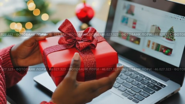 Online shopping at Christmas holidays. Woman buying Xmas gifts online with laptop, sitting next to decorated tree. Female hands hold a cozy red wrapped present among vibrant festive decorations. Стоковое AI-видео, аниматор Марина Демидюк / Фотобанк Лори
