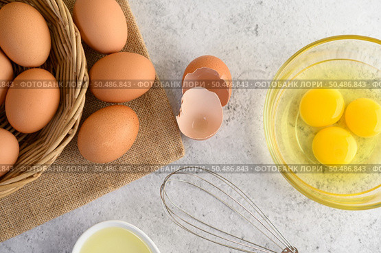 Organic eggs on sack cloth, many eggs on wicker basket and glasses bowl, oil and egg whisk placed on the floor, preparing for cooking food or dessert, copy space. Стоковое фото, агентство Ingram Publishing / Фотобанк Лори