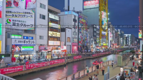 Osaka, Japan - Sep 22 2024, 4k, Panoramic view of Dotonbori river with a ship with tourists, a lot of people on embankment, there are a lot of advertising and illuminations on buildings, Osaka, Japan. Редакционное видео, видеограф Сергей Богомяко / Фотобанк Лори