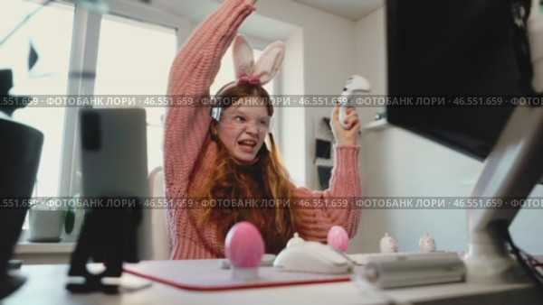 Overjoyed girl raises controller in triumph, celebrating gaming victory. Dressed in bunny ears and LED glasses, she embraces Easter festivity in tech-inspired, modern gaming space. Стоковое видео, видеограф Енваев Андрей / Фотобанк Лори