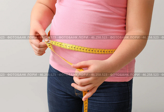 Overweight girl measuring her waist on light background. Стоковое фото, фотограф Pixel_shot / Фотобанк Лори