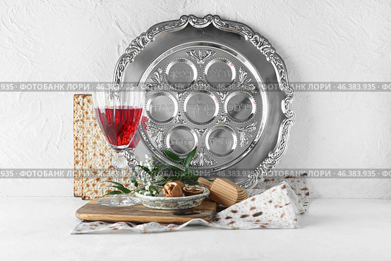 Passover Seder plate with glass of wine, walnuts and matza on white background. Стоковое фото, фотограф Pixel_shot / Фотобанк Лори
