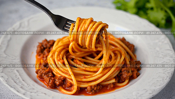 Pasta on a white plate wrapped on a fork in meat tomato sauce. Spaghetti lies on a white plate, screwed onto a fork in a meat sauce. Стоковое AI-изображение, AI-художник Антон Слабоспицкий / Фотобанк Лори