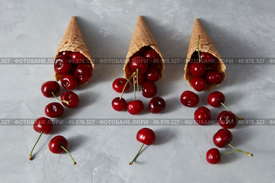 Pattern of freshly picked ripe cherries in a sweet wafer cones on a gray concrete background. Summer concept of homemade ice cream.. Summer fruits pattern with ripe red cherry in a wafer cones on a gray stone table. Стоковое фото, агентство Ingram Publishing / Фотобанк Лори