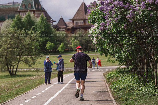 People walk in the park against the background of the palace of Tsar Alexei Mikhailovich in Kolomenskoye. A man does sports running in the park. Russia, Moscow, May 2023. Редакционное фото, фотограф Photojuli / Фотобанк Лори