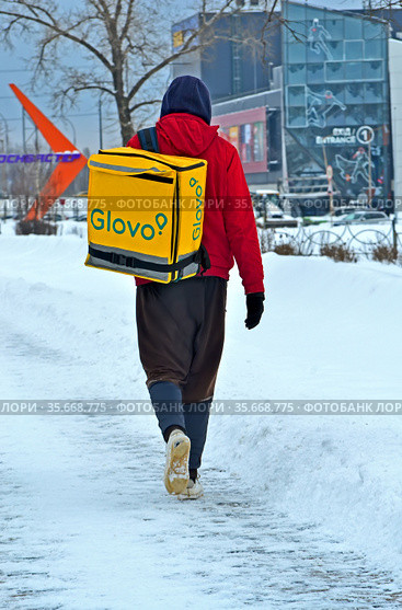 Пеший курьер службы Glovo с желтой термосумкой на улице Киева, Украина (2021 год). Редакционное фото, фотограф FMRU / Фотобанк Лори