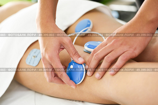 Physiotherapist applying electro stimulation in physical therapy to a young woman. Medical check at the leg in a physiotherapy center. Стоковое фото, агентство Ingram Publishing / Фотобанк Лори