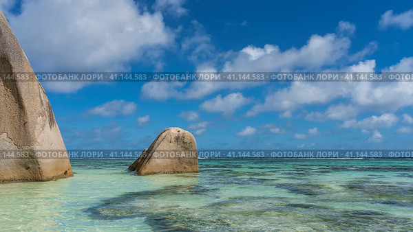 Picturesque granite cliffs rise above the calm turquoise ocean. Steep smoothed slopes. Blue sky with clouds. Seychelles. Anse Source D’Argent beach. La Digue. (2022 год). Стоковое фото, фотограф Вера Ивановна Кубарева / Фотобанк Лори