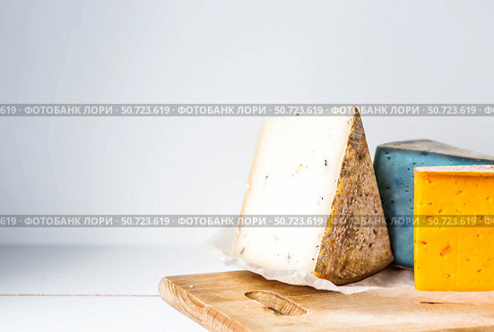 Pieces of fresh, aged, natural farm cheese on parchment paper on a wooden board. Unusual taste and quality of farm-fresh agricultural products. Стоковое фото, фотограф Photojuli / Фотобанк Лори