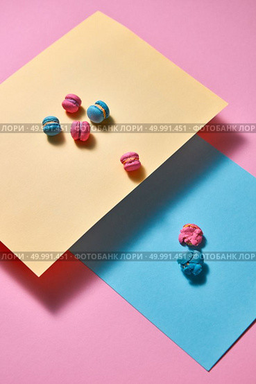 Pink bright macaroons are presented in the form of a triangular pyramid on blue cardboard and one crushed macaroon on a pink paper background with reflection of shadows. Creative composition. composition of colorful macaroons on a blue and yellow papers on pink background. Стоковое фото, агентство Ingram Publishing / Фотобанк Лори