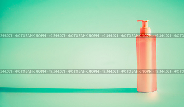 Pink cosmetic bottle with dispenser pump at mint background. Summer skin care lotion or sunblock product with copy space for design. Стоковое фото, агентство Ingram Publishing / Фотобанк Лори