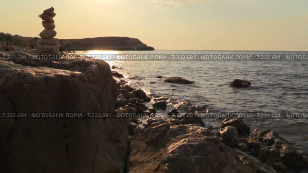 Пирамидка из камней на скалистом берегу моря в лучах заходящего солнца. Стоковое видео, видеограф Арташес Оганджанян / Фотобанк Лори