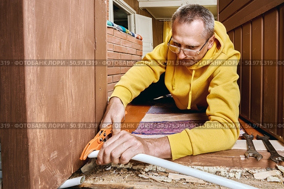 Plumber trims plastic pipe using cutting tool to ensure proper connection surface for placing compression ring and mounting threaded fitting. Стоковое фото, фотограф Владимир Григорьев / Фотобанк Лори