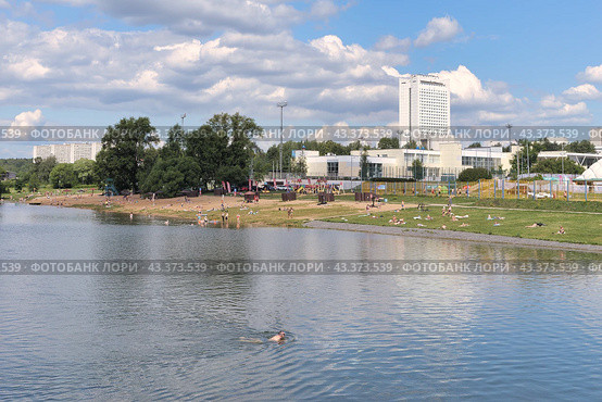 Пляж на городском пруду в Зеленограде. На фоне спортивный комплекс и высотное бизнес центра. Загорающие и купающиеся люди (2024 год). Стоковое фото, фотограф Сергей Никифоров-Гордеев / Фотобанк Лори