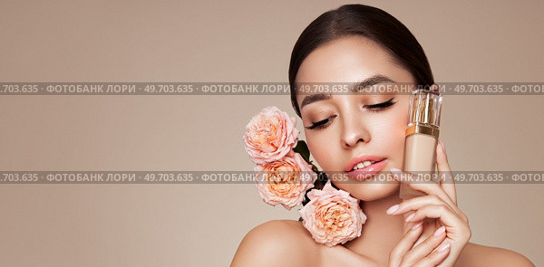 Portrait beautiful young woman with clean fresh skin. Model with foundation makeup bottle. Beautiful young woman with a rose flower. Стоковое фото, агентство Ingram Publishing / Фотобанк Лори