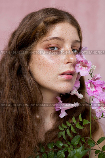 portrait mysterious freckled woman holding pink flower. Стоковое фото, агентство Ingram Publishing / Фотобанк Лори