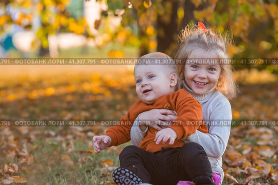 Portrait of a little boy 9 months old and a girl 4 years old outdoors. Happy children are playing in the autumn park. Sister hugs brother. Happy childhood and motherhood. Стоковое фото, фотограф Photojuli / Фотобанк Лори