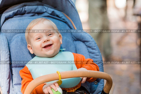 Portrait of a little boy 9 months old in the open air. A happy child in an autumn park is sitting in a stroller. Happy childhood and motherhood. Стоковое фото, фотограф Photojuli / Фотобанк Лори
