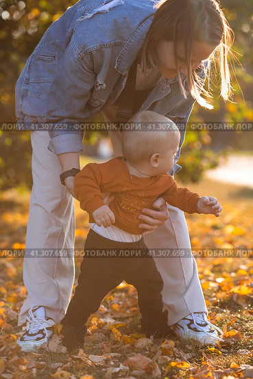 Portrait of a little boy 9 months old in the open air. A happy child in an autumn park takes his first steps. The guy is wearing a bright orange sweater. Happy childhood and motherhood. Стоковое фото, фотограф Photojuli / Фотобанк Лори