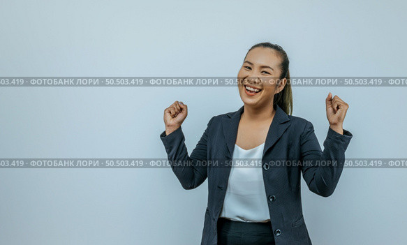 Portrait of Asian woman keeps hands clenched in fists with positiveness as achieved success in career, smiling widely, showing strong powerful, isolated over background with copy space. Стоковое фото, агентство Ingram Publishing / Фотобанк Лори