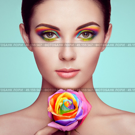 Portrait of beautiful young woman with rainbow rose. Bright colors. Long eyelashes, vivid colorful eyeshadows. Rainbow make up. Multicolored flowers. Стоковое фото, агентство Ingram Publishing / Фотобанк Лори