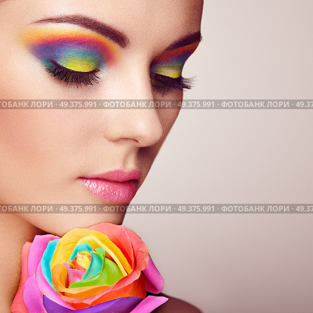 Portrait of beautiful young woman with rainbow rose. Bright colors. Long eyelashes, vivid colorful eyeshadows. Rainbow make up. Multicolored flowers. Стоковое фото, агентство Ingram Publishing / Фотобанк Лори