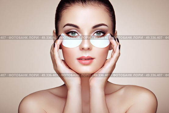 Portrait of Beauty Woman with eye Patches showing an effect of Perfect Skin. Beautiful Face of young Woman with clean Fresh Skin and bare shoulders on beige background. Brunette Spa Girl. Стоковое фото, агентство Ingram Publishing / Фотобанк Лори