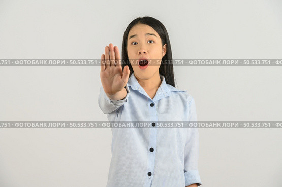 Portrait of Excited young asian woman in blue shirt showing hand foreground and looking at camera isolated on white background. Expression and lifestyle concept. Стоковое фото, агентство Ingram Publishing / Фотобанк Лори