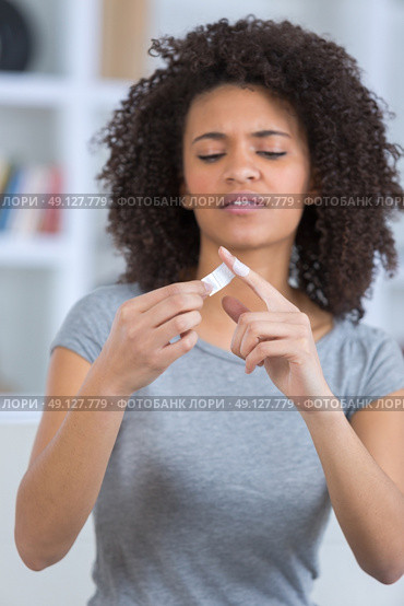 portrait of pretty woman applying bandage on wounded finger. Стоковое фото, агентство Ingram Publishing / Фотобанк Лори