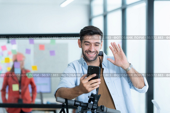 Portrait of smiling businessman talking on mobile phone while colleague using scooter in office. Стоковое фото, агентство Ingram Publishing / Фотобанк Лори