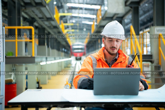Portrait of Young male technician sitting on the table in skytrain repair station, Check the details of the electric train repair in laptop. Стоковое фото, агентство Ingram Publishing / Фотобанк Лори