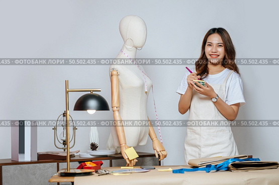 Portrait of young pretty female fashion designer stylish smile during working at fashion studio, Tailor woman’s taking measurements with measuring tape on mannequin in studio at home. Стоковое фото, агентство Ingram Publishing / Фотобанк Лори