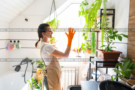 Portrait Woman in rubber gloves and apron manually cleaning in bathroom with rag cleaner and mop inside interior with home plants. Restoring order and cleanliness, cleaning servise. Стоковое фото, фотограф Ольга Симонова / Фотобанк Лори