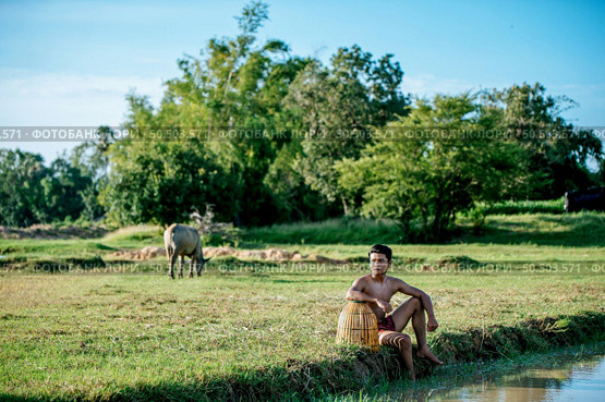 Portrait Young man topless use bamboo fishing trap to catch fish for cooking, Asian young farmer man in rural lifestyle, blurred buffalo is soaking in the swamp. in background. Стоковое фото, агентство Ingram Publishing / Фотобанк Лори
