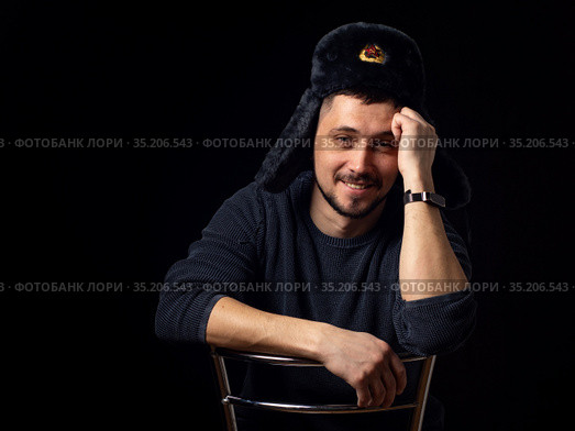 Портрет улыбающегося мужчины тридцати лет кавказской внешности в советской офицерской меховой шапке на черном фоне. Стоковое фото, фотограф Иванов Алексей / Фотобанк Лори