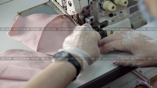 Пошив швейных изделий. Close-up female hands in protective gloves sew a textile product on a sewing machine. Стоковое видео, видеограф EStarodubov / Фотобанк Лори