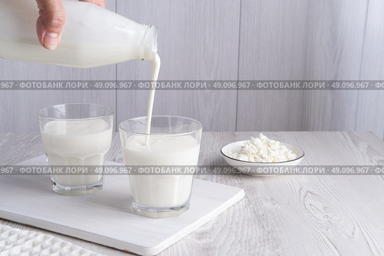 Pouring homemade kefir, buttermilk or yogurt with probiotics. Yogurt flowing from glass bottle on light background. Probiotic cold fermented dairy drink. Trendy food and drink. Copy space. Стоковое фото, фотограф Наталия Попова / Фотобанк Лори