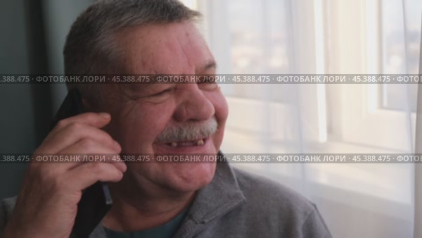 Пожилой мужчина (пенсионер) сидит у окна и разговаривает телефону. Смартфон в руках у пенсионера. Стоковое видео, видеограф Терехова Марина / Фотобанк Лори