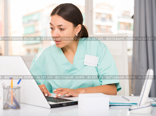 Practicioner girl in medical uniform is working at laptop. Стоковое фото, фотограф Яков Филимонов / Фотобанк Лори