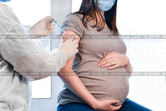 Pregnant Vaccination. Pregnant Woman In Face Mask Getting Vaccinated in Clinic. Doctor Giving Corona Virus Vaccine Injection Patient. Covid-19. Стоковое фото, фотограф Марина Демидюк / Фотобанк Лори