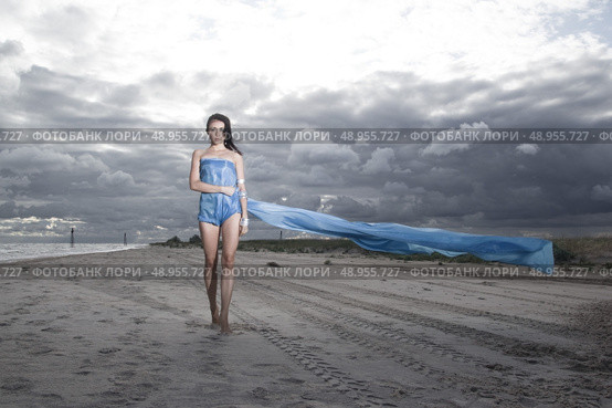 Pretty model holding long blue dress on the beach. Windy and cloudy summer weather. Стоковое фото, агентство Ingram Publishing / Фотобанк Лори
